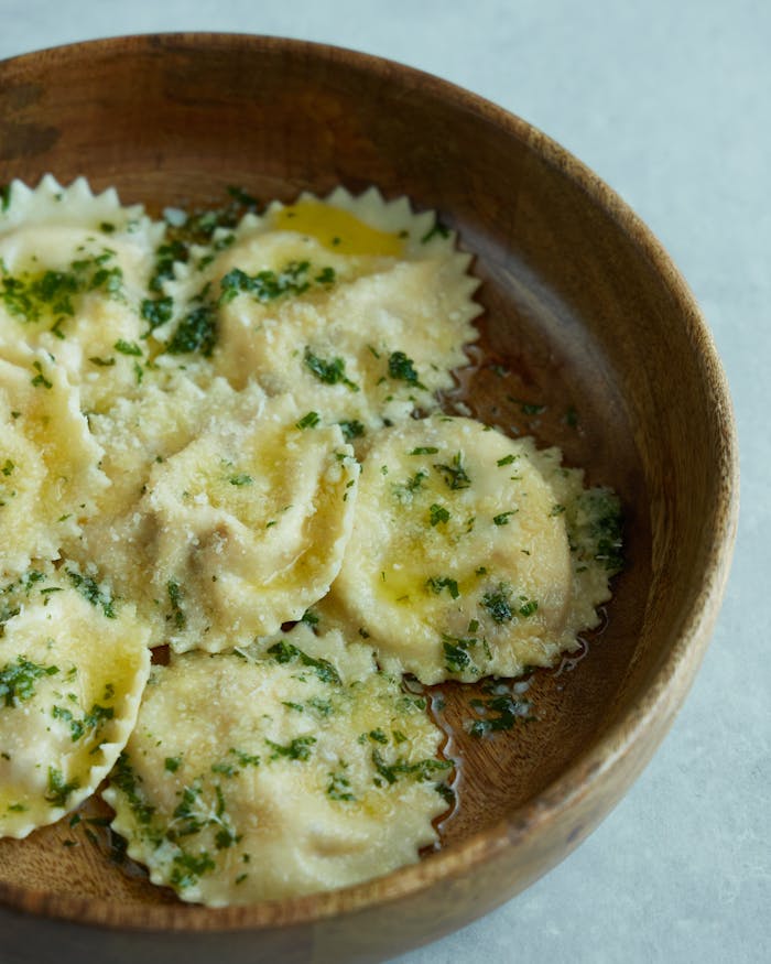Rustic bowl filled with spinach ravioli drizzled with olive oil and herbs.