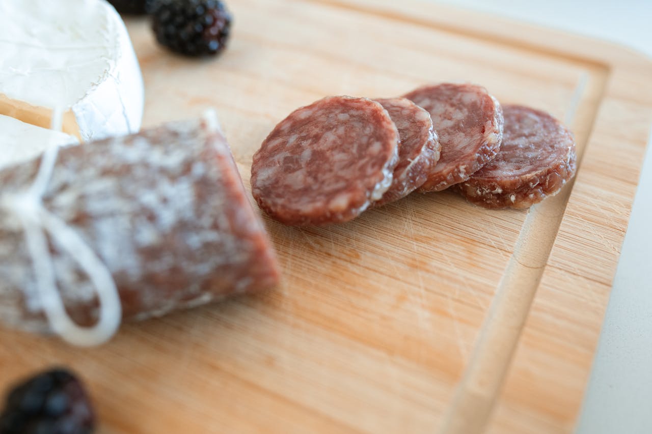 Services-02 Close-up of an artisanal charcuterie board featuring sliced salami, cheese, and fresh blackberries on a wooden cutting board.
