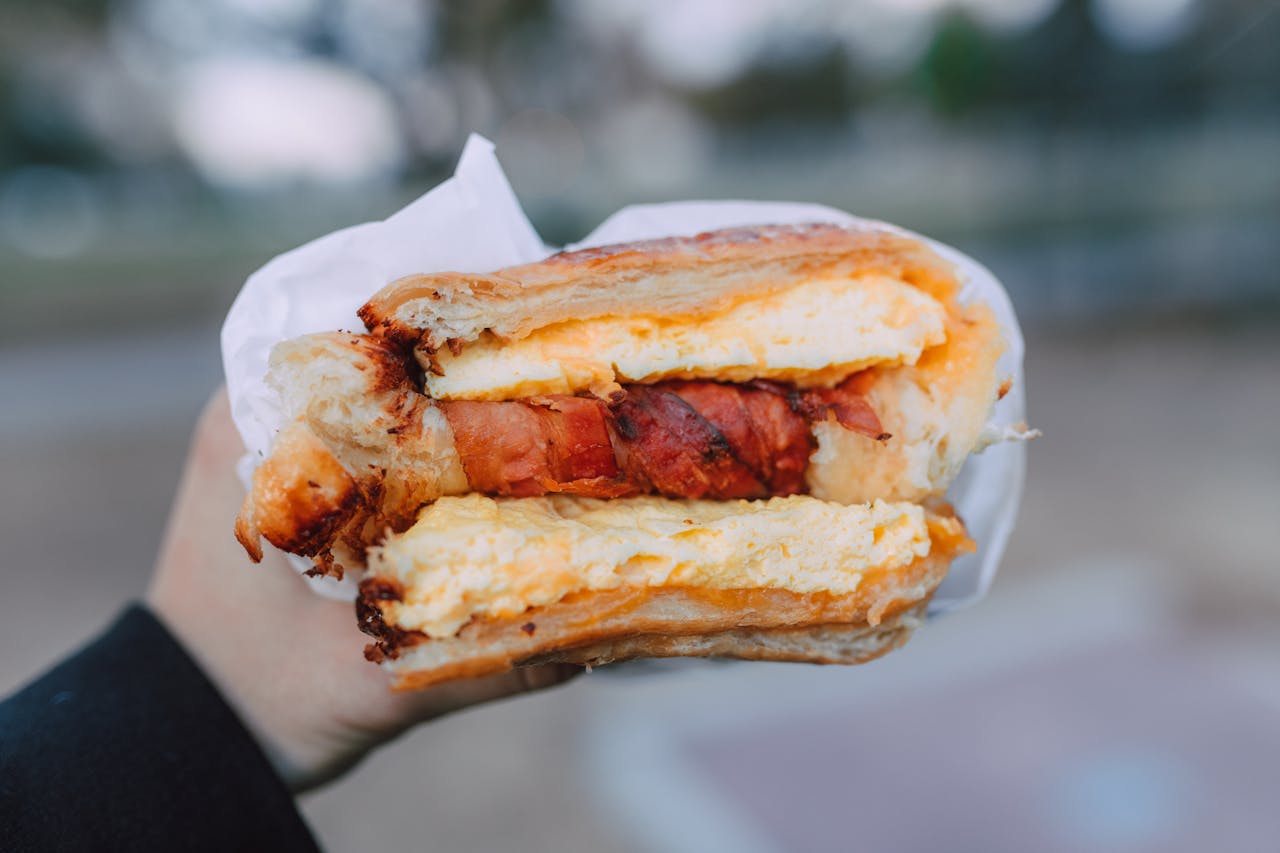 our-story Close-up of a delicious breakfast sandwich with cheese and bacon held outside.