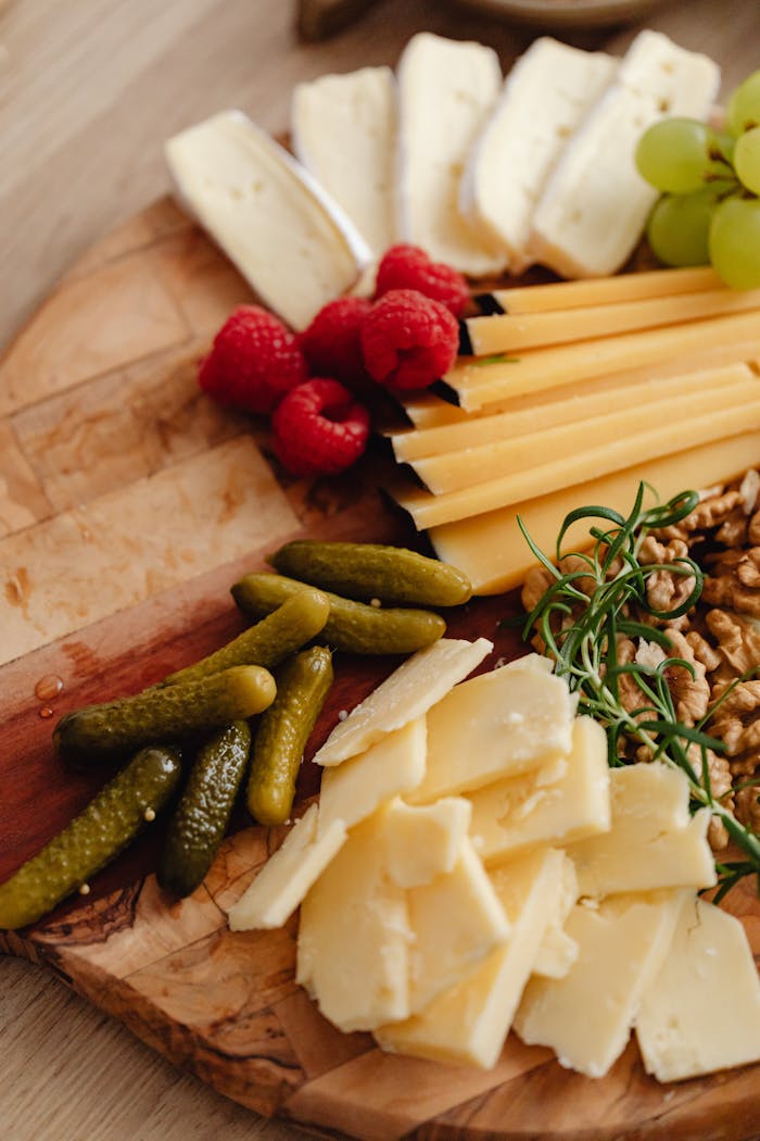 A delectable cheese board featuring cheeses, fruits, pickles, and nuts.