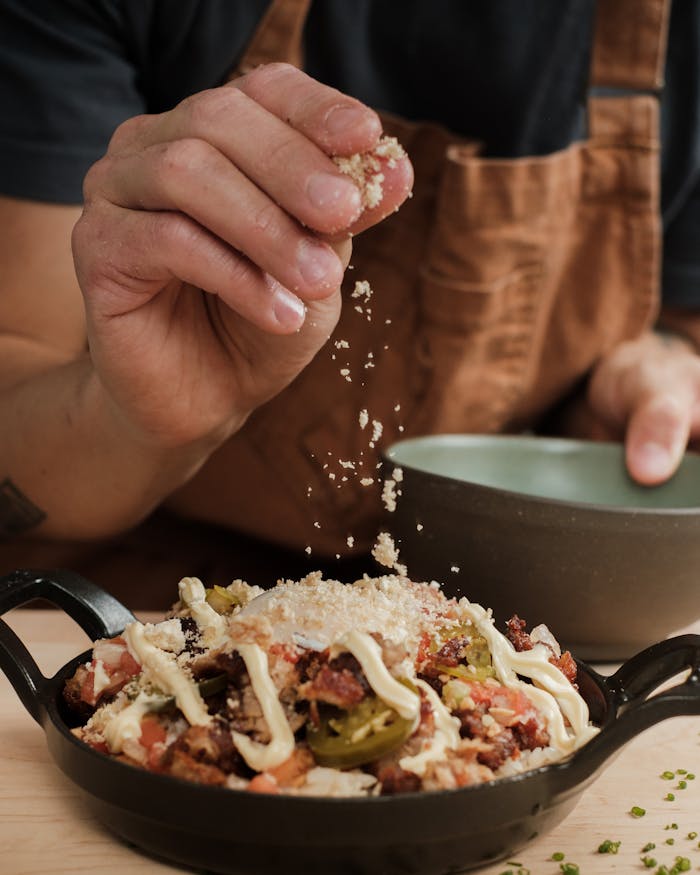 A chef sprinkles cheese on a delicious serving of nachos in a skillet.
