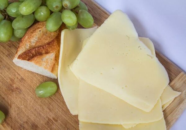Rueda de Queso Manchego junto a varias rebanadas del mismo queso.